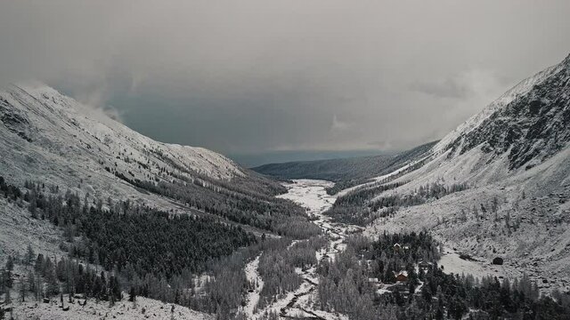 The foot of the glacier of the huge Belukha mountain, the valley of the Aktru River, the Altai mountains. Cloudy weather, storm, wildlife, winter forest, frozen mountain river in the valley of the