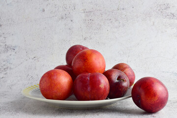Red plums on porcelain plate and stone background. Copy space.