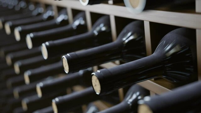 Looping animation of wine bottles ordered on wooden shelves in dark wine-cellar.