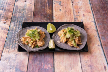 Vegan taco with heura, vegetables, onions and lettuce with parsley and lime for dressing on black plate on wooden table