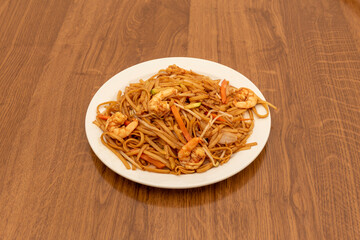 Asian recipe of noodles sautéed with vegetables and prawns with soy sauce on wooden table