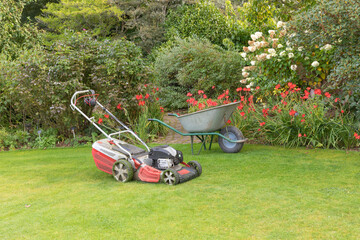 Wheelbarrow and lawnmower ready to be put to work on the garden lawn and flower beds