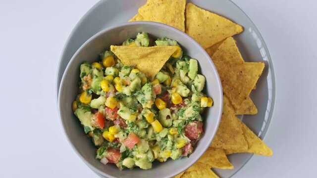 A top rotational view of avocado salad in a gray plate with Doritos on a white table