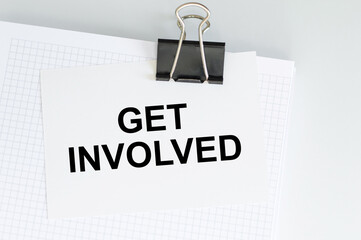 get involved inscription on a card that is attached with a clip to a white notebook on the table