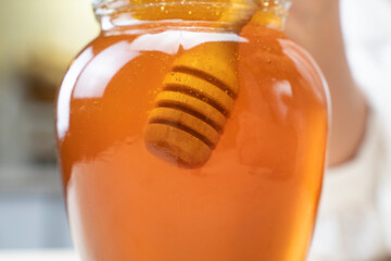 Tastes honey from the jar close up. Girl With wooden spoon pulls out liquid organic honey in a...
