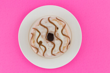 Vanilla striped donut on a white plate isolated on a pink background. Creative food concept with copy space. Top view