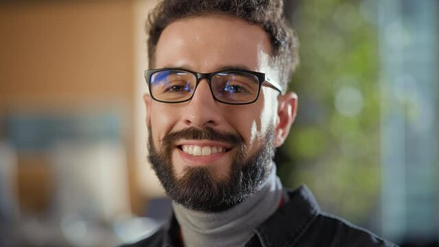 Portrait of a Happy Handsome Smart Male, Charmingly Smiling on Camera Indoors. Confident Successful Man Wears and Turtleneck and Glasses, Has a Bushy Beard and Short Curly Hair.