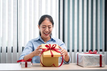 Happy woman is smiling and opening present box with red ribbon while looking into gift box very...