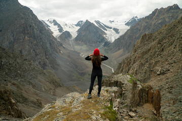 Sports girl in a red hat stands on the top of the mountain