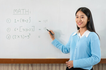 Female tutor standing in front of whiteboard and writing math equations on board to explaining new lesson