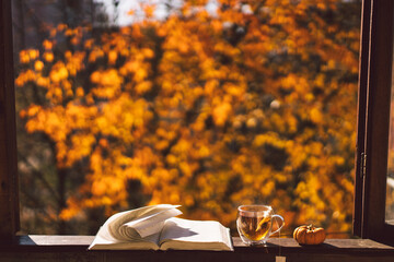 A cup of hot tea and open book on a vintage windowsill. Still life details in home on a wooden window. Read and rest. Cozy autumn concept.