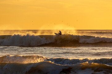 A surfer riding the waves at sunset in Cadiz, Spain.