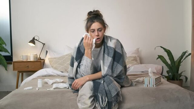 A sick woman wipes her nose with a napkin, and then gets mad because she is tired of being ill at home. An exhausted girl falls on the bed