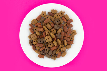 Dry pet food in white plate isolated on pink background. Food for cat and dog. Top view