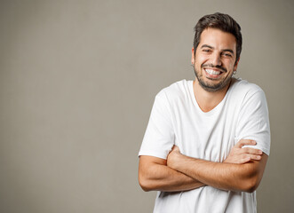 Portrait of handsome smiling man in white t-shirt with crossed arms isolated on gray brownish...