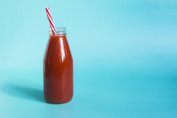 Tomato juice in a transparent bottle with a red tube on a blue background is a place for text