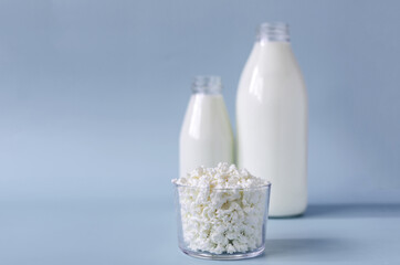 Fresh cottage cheese in a transparent dish on the background of milk bottles, sharpness in the foreground. Cottage cheese in a transparent dish on a blue background is a place for text