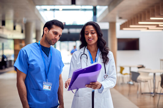 Medical Staff In White Coat And Scrubs Discussing Patient Notes Have Informal Meeting In Hospital