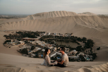 couple sitting in the dunes of Peru with oasis below