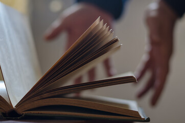 A defocused shot of an old open book and two open male hands. Pa
