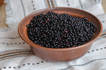 Ripe black elderberries in a brown bowl. Clay bowl on top of a l