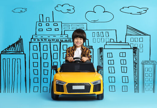 Cute little boy driving toy car and drawing of city on light blue background