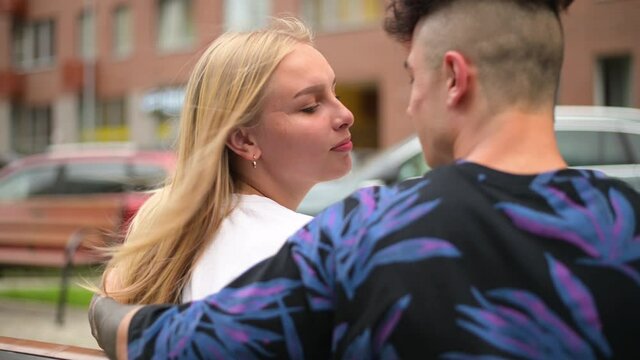 A young couple sits on a bench in the city and communicates, kisses. Meeting and communication of a young man and his girlfriend