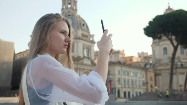 Portrait of Young Tourist woman making a photo of European street at sunrise. Beautiful girl walking through street travelling enjoying summer vacation travel adventure near ruins Rome Italy