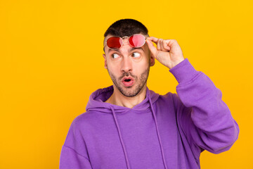 Naklejka premium Photo of impressed millennial brunet guy look empty space wear eyewear purple hoodie isolated on yellow color background