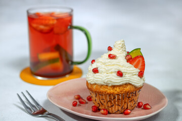 Lemon cupcake with whipped cream and fruit (pomegranate seeds, strawberry, and mango). Fruit tea. 