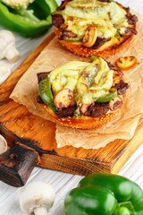 Delicatessen sandwiches on sesame buns halves with beef, bell pepper, onion, mushrooms and cheese on a wooden board on a white background. Rustic style. Selective focus