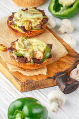 Delicatessen sandwiches on sesame buns halves with beef, bell pepper, onion, mushrooms and cheese on a wooden board on a white background. Rustic style. Selective focus