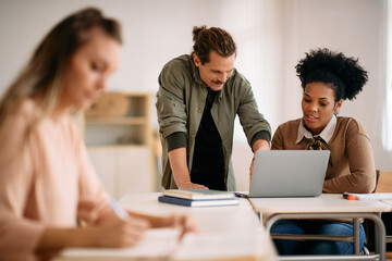 Happy mid adult students collaborate while using laptop in classroom.