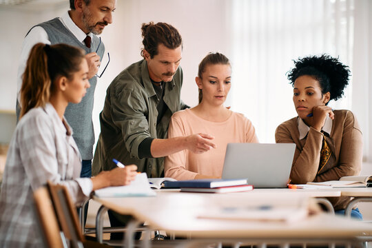 Multi-ethnic group of adult students surfing the net on laptop in classroom.