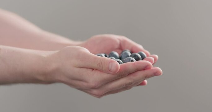 Slow motion man hands show wet washed ripe blueberries on neutral background