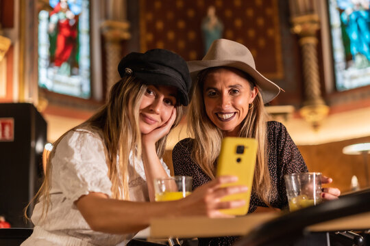 Two friends reading the restaurant menu on the website using a QR. Sipping an orange juice, lifestyle