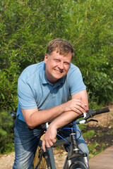 Portrait of an adult male blond 40-44 years old with a wide smile sitting on a bicycle.