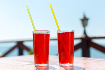 Two glasses with berry juice and strawberries on table of a street cafe against the background of the sea.