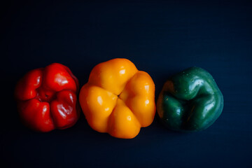 Bulgarian pepper of three colors laid out in a row on black wooden background. Abstract image of traffic light. Concept of healthy eating.