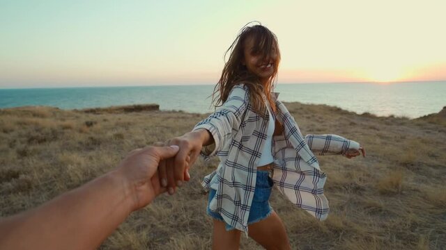 Happy positive emotions girl laughing and holding hand of her friend on cliff with seascape during sunset.