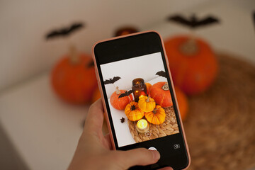 taking a picture on mobile phone of a halloween decoration with orange pumpkins on the kitchen table