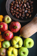 Pan with chestnuts, butternut squash and various fruit on dark background. Flat lay.