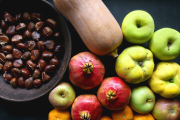 Pan with chestnuts, butternut squash and various fruit on dark background. Flat lay.