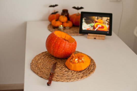 making a jack-o-lantern of an orange pumpkin in the kitchen while watching tutorial on a tablet