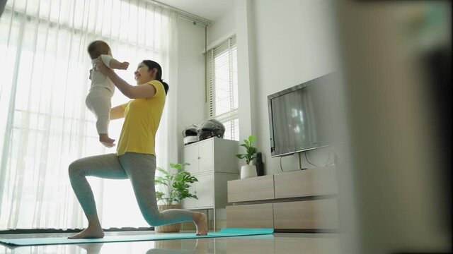 Asian Young mother doing physical yoga exercise with her baby boy at living room.	