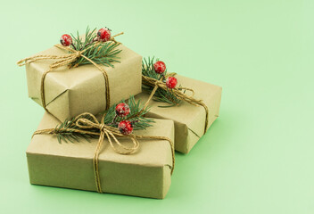 three boxes of gifts in craft paper with decor of spruce branches and berries on a green background.