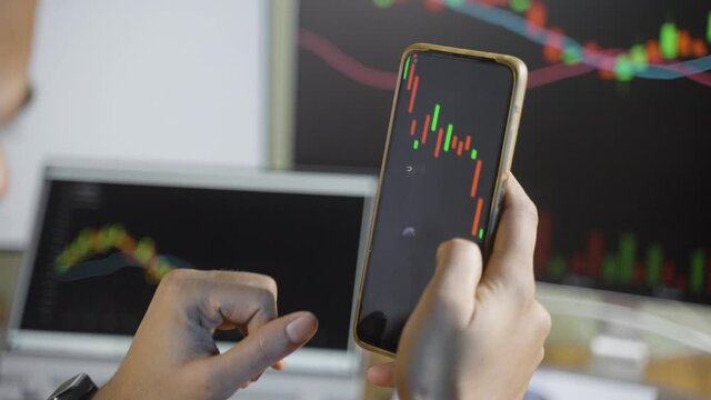 Shoulder shot of trader watching stock market candle stick patterns on mobile phone - concept of Investing money on shares using technical analysis, trading or analyzing on smartphone