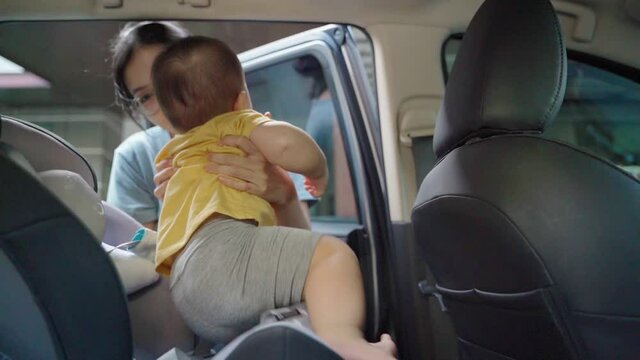 Asian Mother unfastens seat belt of baby car seat.