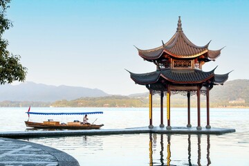 Fototapeta premium Beautiful landscape at Hangzhou West Lake as a rowing boat rows passed the peaceful Jixian Pavilion in the morning