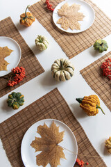 small pumpkins and dry brown maple leafs on white plates, autumn dinner table decors